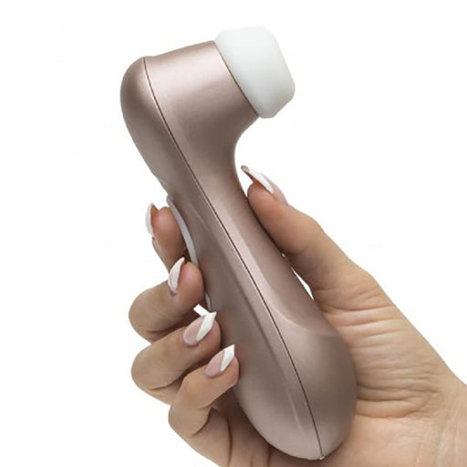 A hand holding the Satisfyer Pro 2 Waterproof Pressure Wave Clitoral Stimulator, a rose gold-colored electronic device with a rounded white tip. The person has neatly manicured nails painted in a pale pink shade.