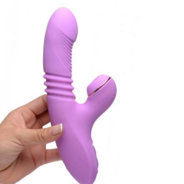 A hand holds the Shegasm Thrusting & Clitoral Air Pulsation Rabbit Vibrator by XR Brands. This purple luxury toy boasts a ribbed shaft and a smaller, curved clitoral stimulator for external pleasure. Crafted from smooth silicone and ABS plastic, its tip is slightly rounded for added comfort.