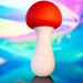 The Shroomie Mushroom Shaped Mini Wand Vibrator by Maia Toys, featuring a red top and white base with two buttons, is set against a vibrant, colorful background. The base bears the Maia name and offers waterproof and vibrating functions. This delightful creation from Trippy Toys adds excitement to any collection.