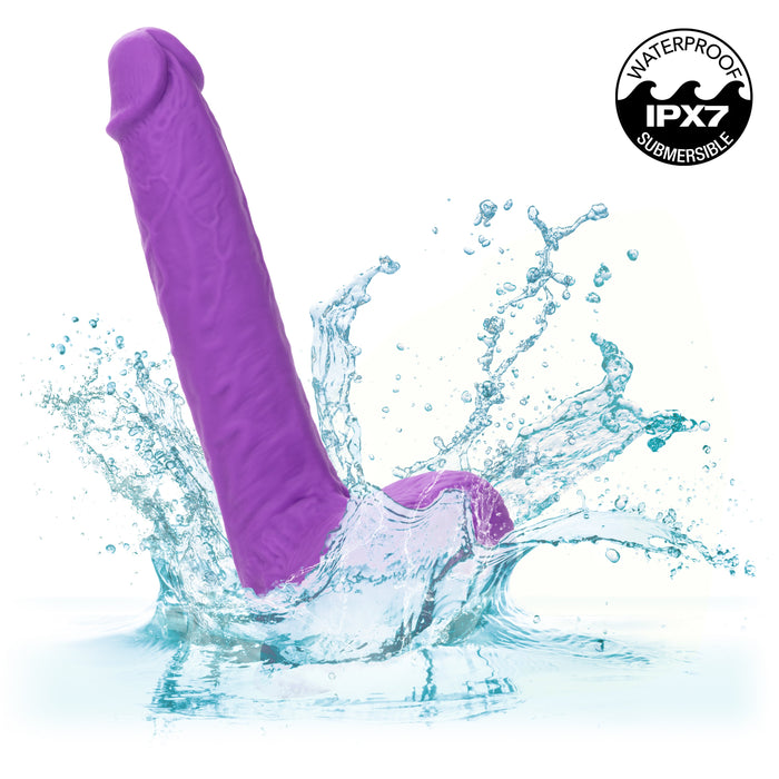 A pink, vibrating dildo splashing into water with droplets all around. The image includes a logo in the top right that reads "WATERPROOF IPX7 SUBMERSIBLE." Crafted from silky silicone for intense action, this is the CalExotics Silicone Stud Rumbling & Thrusting 9.5 Inch Dildo.