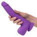 A hand holding the Silicone Stud Rumbling & Thrusting 9.5 Inch Pink Dildo by CalExotics is shown. The silky silicone dildo features a textured shaft and well-defined head, reflecting its lifelike design, while its suction cup base adds versatility. The plain white background highlights the detail and vibrant pink color of the object.