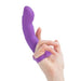 A person's hand holding a purple Simple and True Silicone G-Spot Finger Extender by BMS Enterprises, with their index and middle fingers inserted into the Extra Touch Finger loop at the base of the toy. The background is plain white.