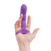 A hand holding the Simple and True Silicone G-Spot Finger Extender - Purple by BMS Enterprises. The toy, designed to be worn on the finger, features a bulbous, ribbed tip made of soft silicone for a stimulating texture. It also has a textured triangular base for added stimulation.