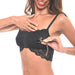 A person with long hair wears a black lace bralette with a front clasp and is touching their collarbone. They are smiling and using Sportsheets' Sincerely Amber Beaded Nipple Clamps attached to a chain, holding it in their left hand near the bra's front clasp.