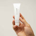 A hand holding a small white tube of "Slow Sex Finger Play Gel for Fingering" by Bijoux Indiscrets. The label also reads "Finger Play Gel" and "30 ml = 1 fl. oz." This masturbation gel features natural lubrication with a hint of coconut aroma. The background is plain and light.