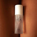 A bottle of "Slow Sex Full Body Massage Gel" by Bijoux Indiscrets, infused with a coconut scent, is placed upright on a surface with a peach-toned, flesh-like texture in the background. The sleek, semi-transparent bottle with a white cap promises body-on-body fun. The text on the bottle is clearly visible.