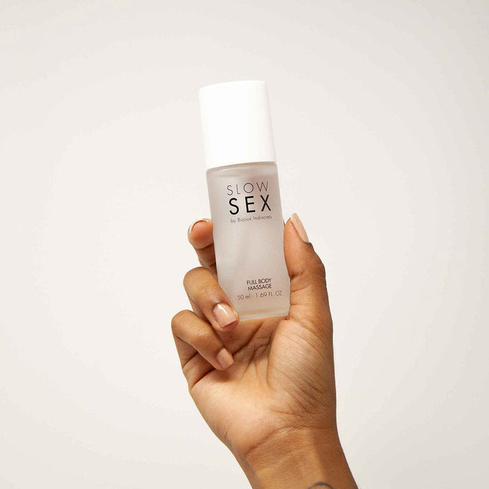 A hand is holding a small white bottle labeled "Bijoux Indiscrets Slow Sex Full Body Massage Gel 50 ml / 1.69 fl oz" against a plain background, promising an enticing full-body massage experience.