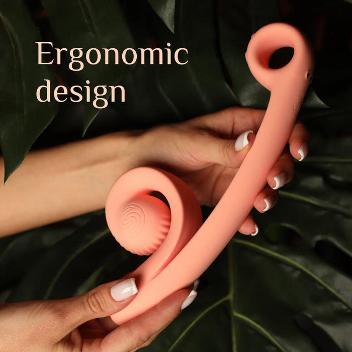 Two hands hold a peach-colored, S-shaped Snail Vibe Curve Ultra Powerful 2 Motor Dual Stimulating Vibrator with an ergonomic shape against a backdrop of green leaves. The device features a ribbed, spherical end and a smooth handle with a circular opening at the top. Text on the image reads "Snail Vibe Curve: Ergonomic design.