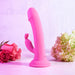 An Evolved Novelties Somebunny to Love Uncut Look Rabbit Vibrator, made from pink silicone and equipped with powerful motors, stands upright on a light pink surface. In the background, pink and white roses are arranged on one side while a white hydrangea bouquet adorns the other, all set against a softly focused pinkish backdrop.