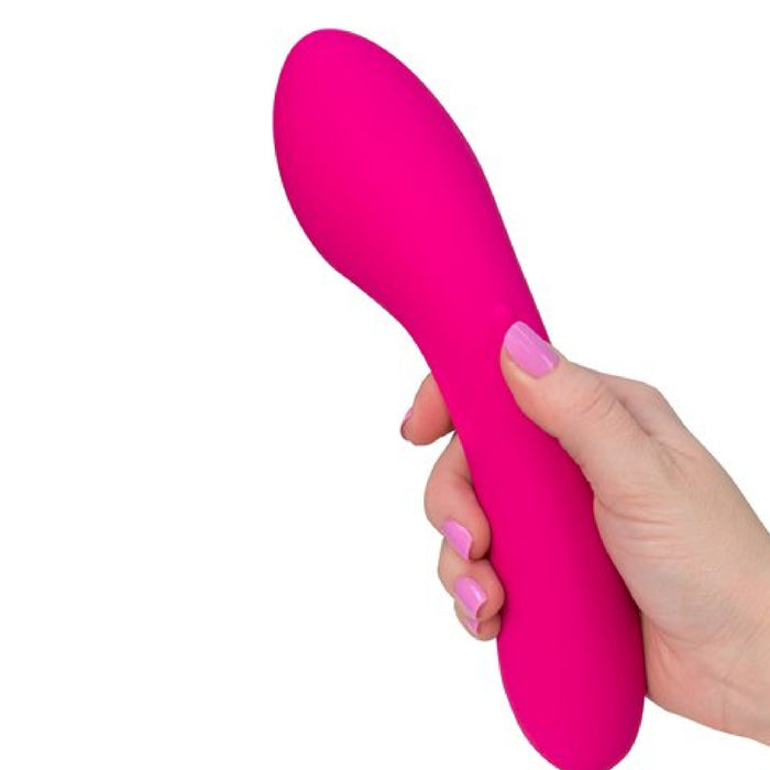 A person with light skin is holding the Swan Wand Powerful Rumbly Double Ended 2 Motor Vibrator by BMS Enterprises, a bright pink, curved wand made of 100% silicone, in their hand. The object features a cylindrical end and a rounded, bulbous shape at the opposite end. The background is white, and the person's nails are painted light pink.