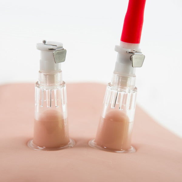 Two clear plastic medical connectors from the Temptasia Beginner's Breast and Clitoral Pumping System by Blush are attached to a simulated skin surface, bearing red and white tubes at the top. Likely used for training or demonstration purposes, these devices could intriguingly double as components in an advanced nipple pump system for enhanced pleasure scenarios.