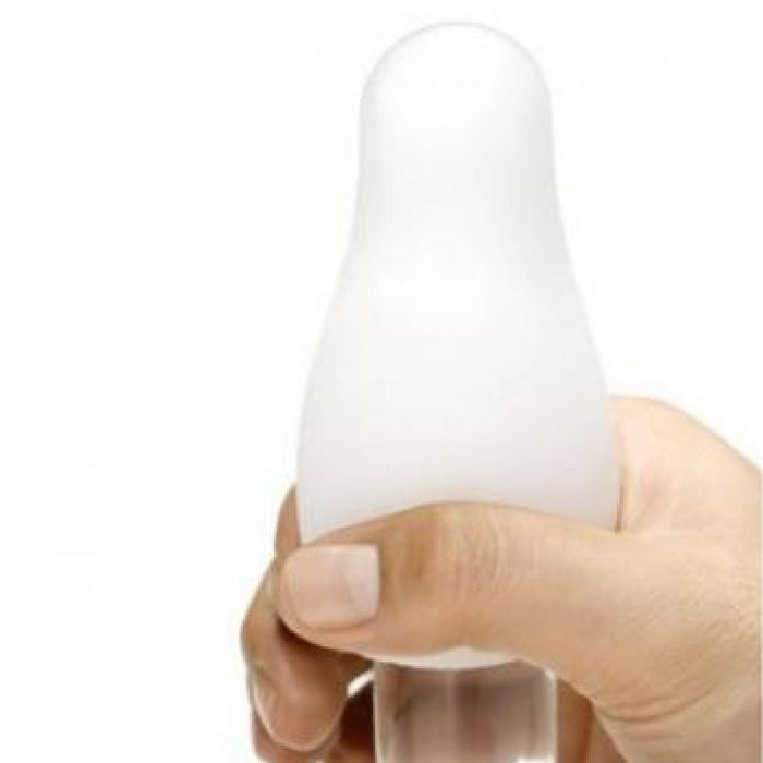 A hand holds a white, rounded, bulb-like object reminiscent of a Tenga Egg Disposable Penis Masturbator - Wavy 2's top. The fingers grip the clear base against a plain white background, capturing an intimate travel buddy moment.