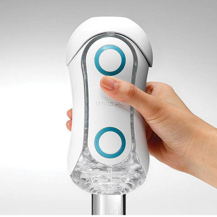 A hand is holding a sleek, white Tenga Flip Orb Penis Masturbator - Blue Rush device, featuring two blue circular buttons on its front. The curved, futuristic design includes a clear compartment at the bottom and an adjustable pad for comfort. The brand name "Tenga" is prominently displayed in the center.