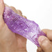 A hand stretching a translucent purple Tenga Uni Topaz Textured Finger Sleeve, showcasing its elasticity and textured surface against a white background.