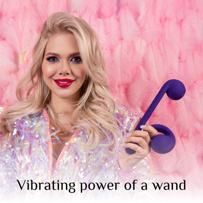 A blonde woman with vibrant makeup and a shimmering outfit smiles while holding The Snail Ultra Powerful 2 Motor Dual Stimulating Vibrator - Purple. The background is adorned with pink feathers. The text at the bottom of the image reads, "Vibrating power of a wand.