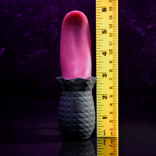 The Evolved Novelties Tongue Teaser Flickering Realistic Red Tongue Vibrator stands upright next to a yellow measuring ruler against a dark purple background. Offering realistic oral sensations, the ruler shows it is around 6 inches tall. This enticing, waterproof, and submersible toy promises endless pleasure.