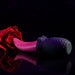 A red rose intertwined with the Evolved Novelties Tongue Teaser Flickering Realistic Red Tongue Vibrator, set against a dark background. The image reflects a blend of romantic and sensual themes, showcasing the allure of realistic oral sensations with its pink and black textured, flexible design.