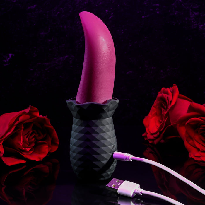 The Tongue Teaser Flickering Realistic Red Tongue Vibrator by Evolved Novelties is shown in a striking scene. The pink, curved adult toy with its textured black base is positioned against a dark background adorned with deep red roses. Connected via a white USB cable, the flexible tongue vibrator exudes hints of realistic oral sensations under a soft purple light.