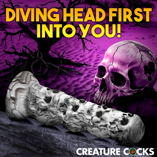 An image showcasing a promotional graphic with the text "Diving Head First Into You!" in bold, yellow letters at the top. Below, the Tower of Doom Silicone Skull Dildo by XR Brands is displayed against a purple background featuring a spooky skull and tree. The words "Creature Cocks" are positioned at the bottom right.