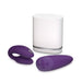 A set of purple electronic devices from We-Vibe, including the We-Vibe Chorus Remote & App Controlled Couples' Vibrator and a handheld remote control, is placed on a white surface. The items are accompanied by a white rectangular charging or storage unit.