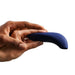 A hand holds the We-Vibe Melt Rechargeable Pleasure Air Clitoral Stimulator in blue, a sleek and ergonomic device with a narrow tip and wider base. It has a smooth, matte finish and is palm-sized, designed specifically for clitoral air pulse stimulation. The background is plain white.