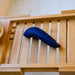 The We-Vibe Melt Rechargeable Pleasure Air Clitoral Stimulator in blue rests on a rectangular wooden slatted tray, likely part of a bath caddy. A small brush with white bristles is partially visible on the left side. This versatile device can be paired with the We-Connect app for enhanced pleasure air or clitoral air pulse stimulation experiences.