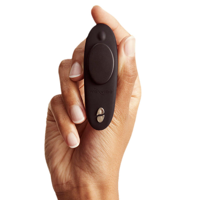 A hand is holding a small, black, oval-shaped electronic device with buttons on it. The sleek design of this We-Vibe Moxie + Hands-Free Remote or App Controlled Panty Vibrator makes it both discreet and effective for use.