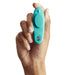 A hand holds the We-Vibe Moxie + Hands-Free Remote or App Controlled Panty Vibrator in teal, a small wearable device designed for clitoral stimulation. The We-Vibe features an oval, slightly indented surface on one side, with buttons and a small opening near the bottom. The white background highlights both the hand and the remote-controlled vibrator.