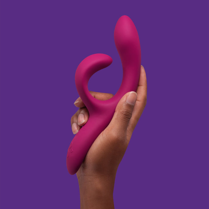 A hand holding the We-Vibe Nova 2 Powerful Flexible G-Spot Rabbit Vibrator against a solid purple background. The vibrator, featuring an adjustable G-spot arm, has a curved shape designed for both internal and external stimulation.