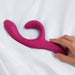 A hand holds the We-Vibe Nova 2 Powerful Flexible G-Spot Rabbit Vibrator in pink silicone on a white fabric background.