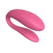 The We-Vibe Sync Lite App Controlled Wearable Couples Vibrator in pink features a curved, smooth, and streamlined design with textured ridges on one end. It includes a control button at the top and is ergonomically designed for comfort and ease of use, making it ideal for shared experiences. The background is white.