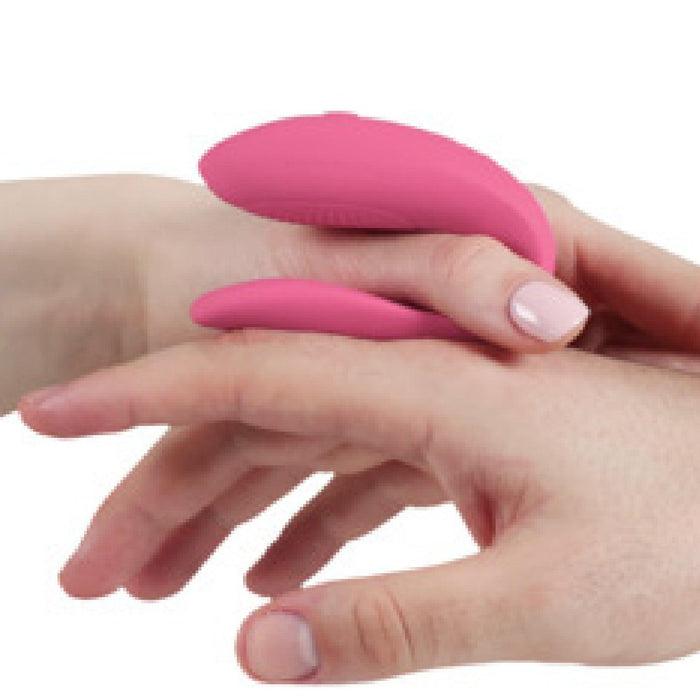 Close-up of two hands holding a We-Vibe Sync Lite App Controlled Wearable Couples Vibrator - Pink with a smooth surface. The object is being gently held between the fingers. The background is plain white, and the hands are positioned to show the shape and size of the pink couples vibrator from We-Vibe.