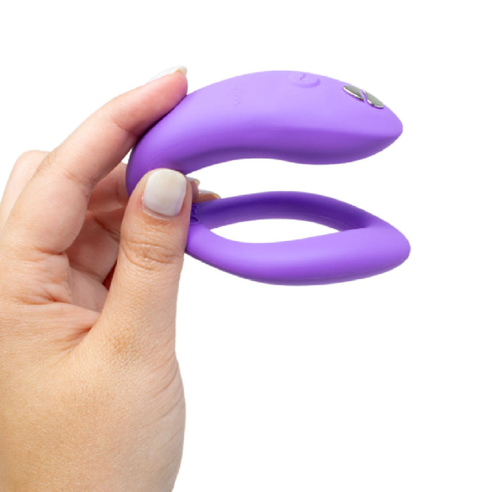 A hand holding the We-Vibe Sync O Hands-Free Wearable Couples Vibrator in purple, showcasing its U-shaped design, smooth texture, and button controls on one end. This flexible, waterproof device is compact and ideal for use as a wearable couples vibe.