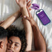 A couple lies in bed facing each other with their eyes closed, the woman's arms stretched above her head. Beside them on the bed, a smartphone displays "SYNC" on the screen next to a purple, waterproof We-Vibe Sync O Hands-Free Wearable Couples Vibrator designed for app control.