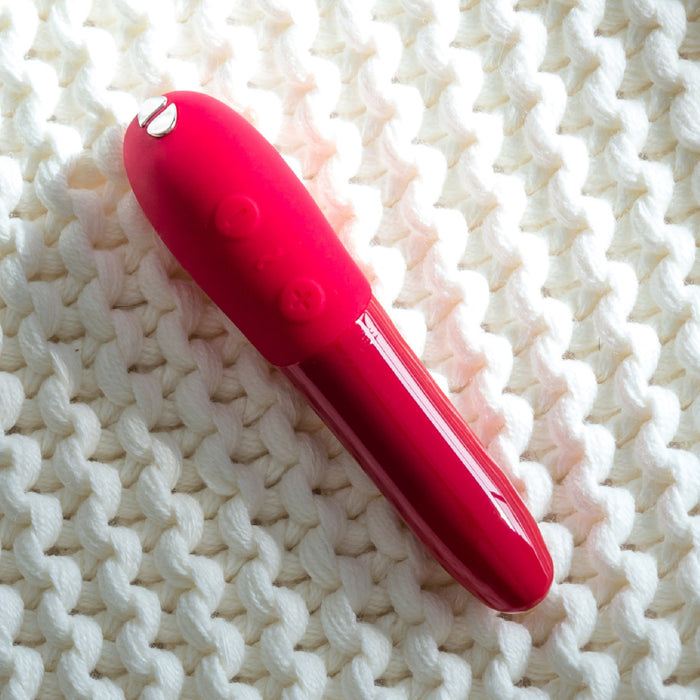 A We-Vibe Tango X Powerful Bullet Vibrator - Red lies on a white knitted fabric background. The vibrator, reminiscent of a discreet lip balm tube, has a glossy cap and a textured body with raised circular and star-shaped designs.