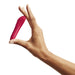 A person is holding a We-Vibe Tango X Powerful Bullet Vibrator - Red, shaped like a lipstick tube, between their thumb and index finger against a plain white background.