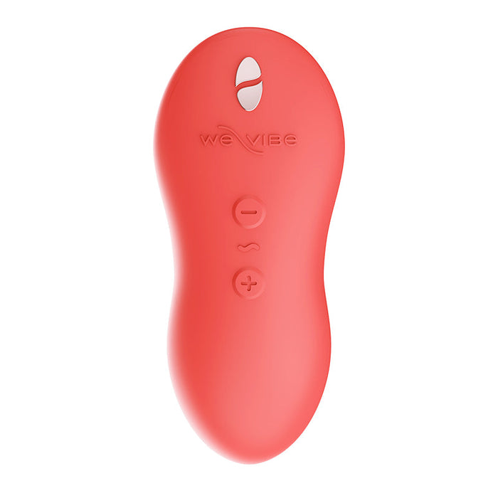 A coral-colored, ergonomically-shaped remote control for the We-Vibe Touch X Lay On Vibrator with three vertically arranged buttons: a wavy line in the center, a minus sign above it, and a plus sign below. The word "WE VIBE" is embossed above the buttons, with a small cutout at the top revealing part of a loop.