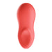 A smooth, coral-colored, oval-shaped We-Vibe Touch X lay on vibrator with a slight depression near the base. The sleek, solid design and silicone coating suggest it is a sophisticated tool. The object is photographed against a plain white background.