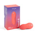 The image shows a Coral We-Vibe Touch X Lay On Vibrator placed next to its packaging box. The box is predominantly purple with red accents and has text reading "Magic Multitasker" and "Touch X" on it. The compact, sleek design features a waterproof silicone coating and three control buttons.