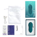 A green We-Vibe Touch X Lay On Vibrator by We-Vibe is shown along with its box, white storage pouch, USB charging cable, and user manuals. Featuring a waterproof silicone coating, it also includes a small sachet of We-Vibe lube and a packet from Pjur.