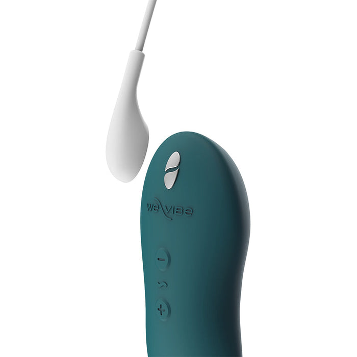 Close-up of a green-colored remote control for a personal care device, featuring three buttons labeled with plus, minus, and a diamond shape. The waterproof We-Vibe Touch X Lay On Vibrator is attached via a white cord leading to a small white sensor or attachment, all enhanced with silicone coating.