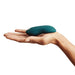 A We-Vibe Touch X Lay On Vibrator in green is being held in the palm of a person's hand against a plain white background. The smooth, curved device features a silicone coating that fits comfortably in the hand.