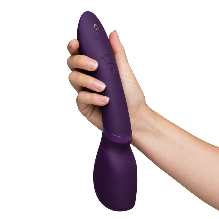 A hand holds the We-Vibe Wand 2, a sleek and curved purple cordless vibrator with button controls, showcasing its sophisticated design.