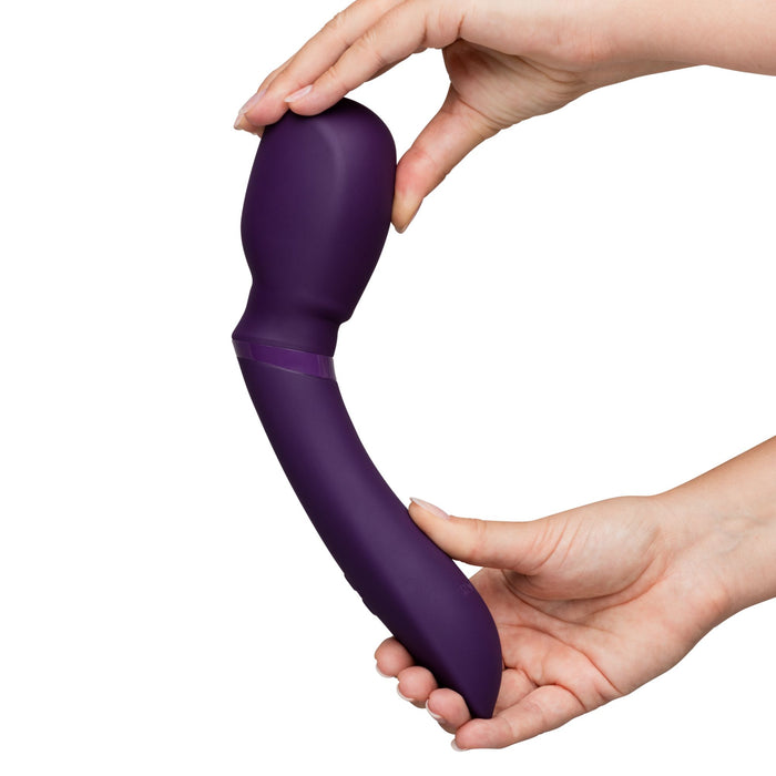 A person holds the We-Vibe Wand 2 Powerful Cordless Splashproof App Enabled Vibrator, which has a purple, curved design, with both hands. The wand vibrator from We-Vibe features a smooth texture and a bulbous head. The background is plain white.