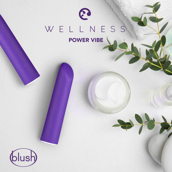 A promotional image for the Blush "Wellness Power Bullet - Rumbly Waterproof Ultra Strong Vibrator" showcases the purple vibrator next to a white jar and green eucalyptus branches. The background displays rolled white towels that are partially visible in the top right corner against a light-colored backdrop.