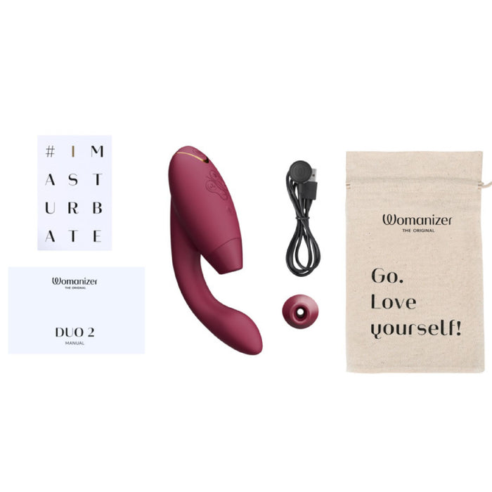 Image of the Womanizer Duo 2 Pleasure Air Clitoral & G-Spot Rabbit in Bordeaux, a personal pleasure device by Womanizer featuring clitoral air pulsation and G-spot vibration. The set includes the main device, charging cable, additional nozzle, manual, postcard with "#IMASTURBATE," and a beige storage bag with "Go. Love yourself!" printed on it.