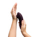 A person holds a plum-colored, ergonomically designed Womanizer Next Pleasure Air Clitoral Vibrator by Womanizer, pressing it against the palm of their other hand with fingers curved around its contoured shape. The innovative Pleasure Air Technology promises unparalleled clitoral stimulation. The background is white.