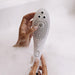 A person holding the Womanizer Wave Water Pulsing Shower Masturbator (White) from the brand Womanizer. The device features multiple spray nozzles and a button on the handle. The water massager is enveloped in soapy bubbles, and soap suds partially cover the person's hands.