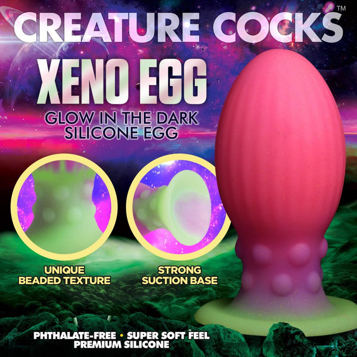 Promotional image for the "Xeno Egg Glow In The Dark Extra Large Silicone Egg" by XR Brands. This pink egg with a green base, crafted from premium silicone, features ribbed sides and a strong suction base. Set against a vibrant, otherworldly landscape, bold text highlights the product's unique attributes.