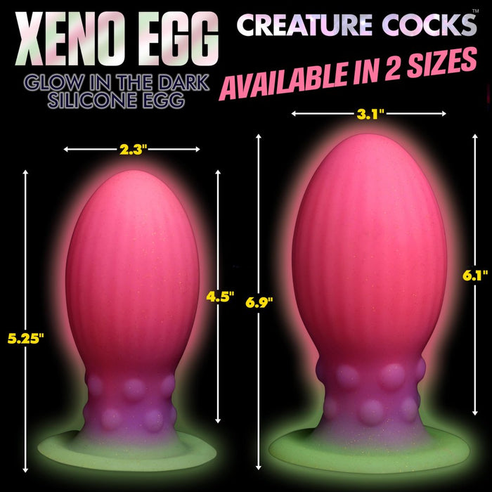 An image featuring two premium silicone products from XR Brands, named "Xeno Egg Glow In The Dark Extra Large Silicone Egg." These come in two sizes: the smaller one is 2.3 inches wide and 5.25 inches tall, while the larger one measures 3.1 inches wide and 6.9 inches tall. Both sizes boast ribbed sides and a glow-in-the-dark feature for added allure.